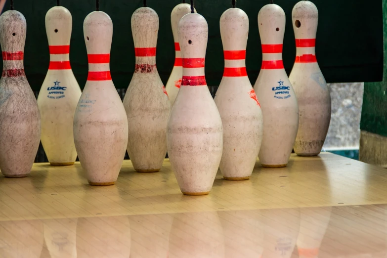 a row of bowling pins sitting on top of a wooden table, a picture, by Raymond Normand, very wide wide shot, nets, usa-sep 20, white and red color scheme