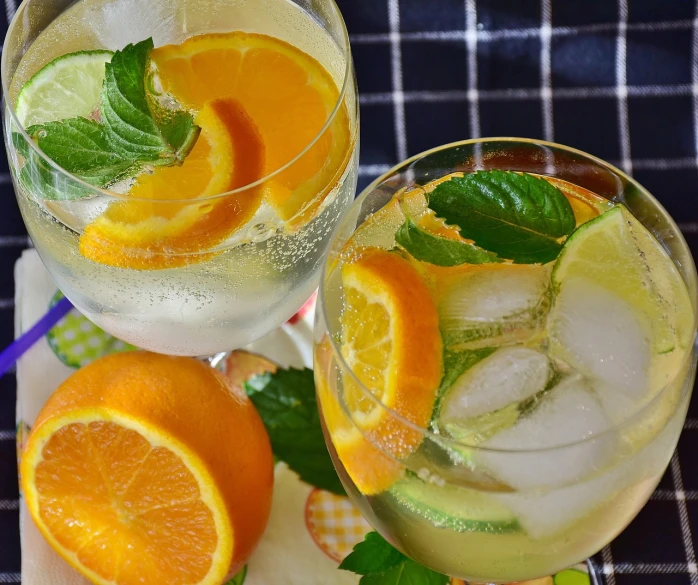 a couple of glasses filled with drinks sitting on top of a table, by Anna Findlay, pexels, orange slices, mint, aspic, detailed water