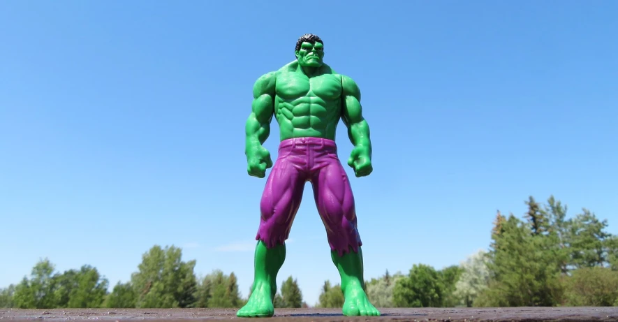 a close up of a toy figure of a hulk, by Arnie Swekel, pexels, figuration libre, full body full height, green and purple, posing like a superhero, standing on rocky ground