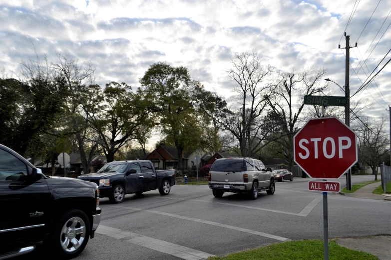 a red stop sign sitting on the side of a road, by Linda Sutton, 5 hotrods driving down a street, tyler, intersection, residential