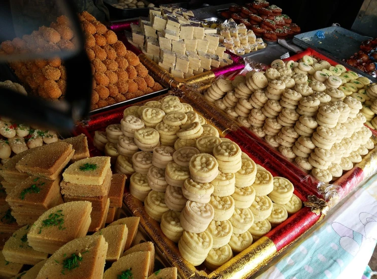 a table topped with lots of different types of cookies, by Bernardino Mei, hurufiyya, on an indian street, beautiful composition, many golden layers, fanoos