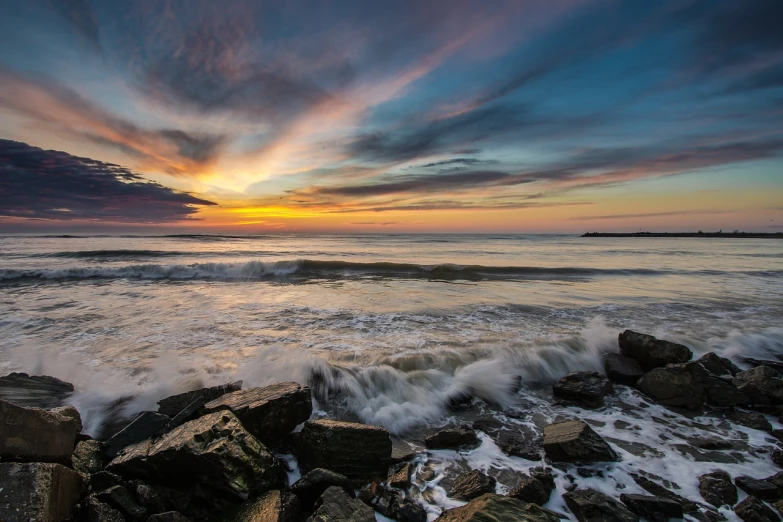 a sunset over the ocean with rocks in the foreground, a picture, by Jeffrey Smith, crashing waves and sea foam, rhode island, clouds and waves, vivid lines