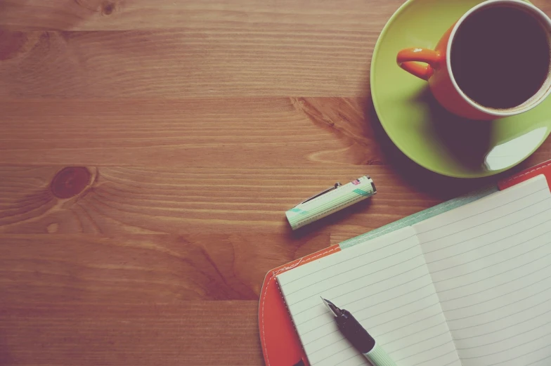 a cup of coffee sitting on top of a wooden table, a sketch, pexels, green and orange theme, retro effect, notebook, set photo