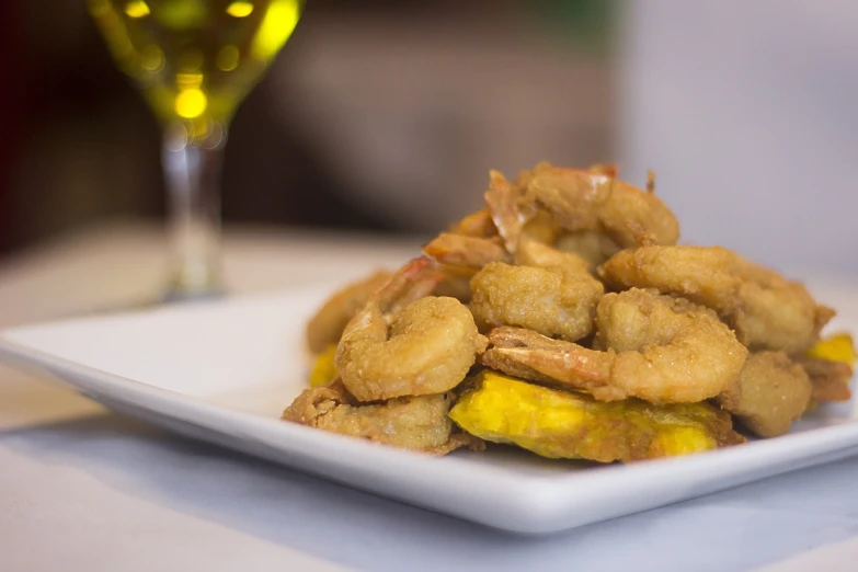 a white plate topped with fried food next to a glass of wine, by Matt Cavotta, flickr, shrimp, banana, stacked image, spain