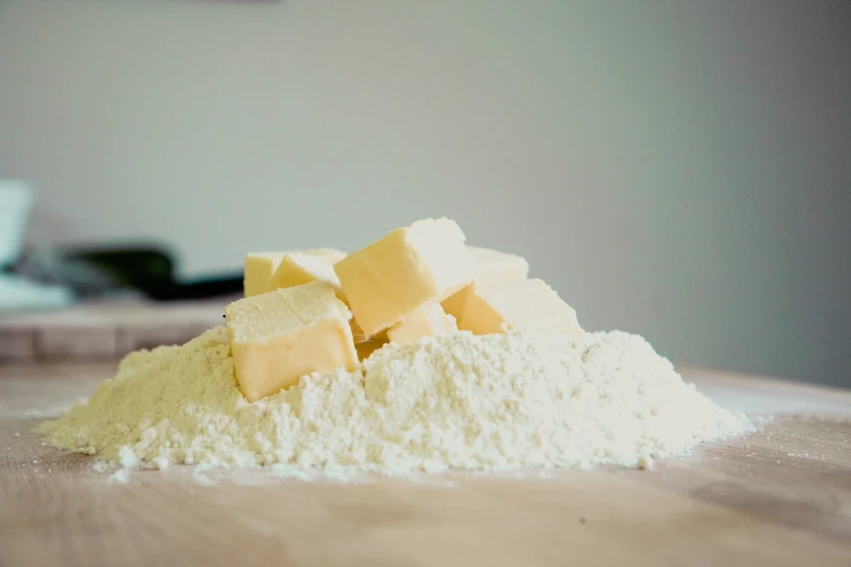 a pile of butter sitting on top of a wooden table, a picture, by Karl Buesgen, pexels, visual art, covered in white flour, local foods, on a pale background, looking partly to the left
