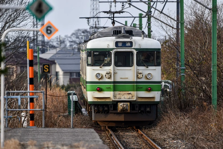 a green and white train traveling down train tracks, shin hanga, frontshot, yard, run down, february)