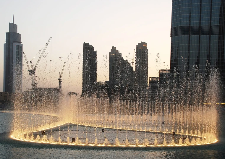 a fountain of water with a city in the background, a picture, hurufiyya, entertainment district, during golden hour, sheikh mohammed ruler of dubai, construction