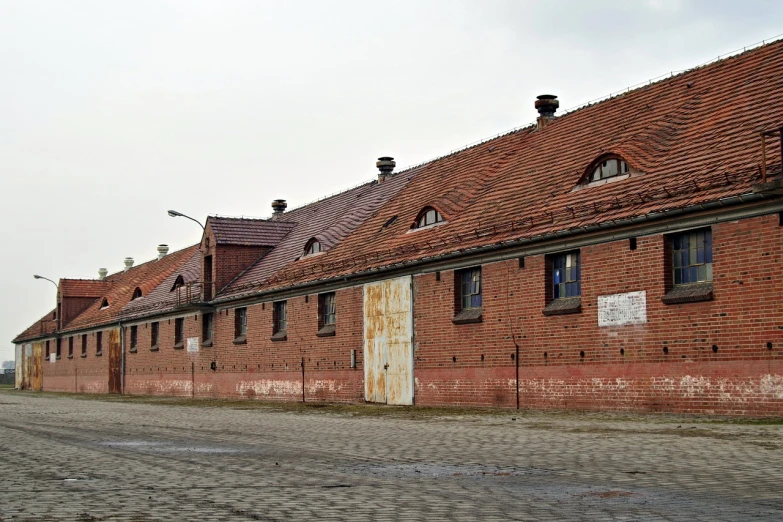 a red brick building sitting on the side of a road, a photo, by Karl Völker, auschwitz camp, hangar, white buildings with red roofs, anato finnstark. front view