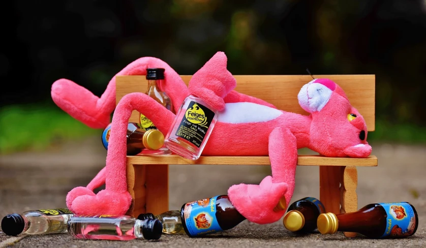 a pink stuffed animal laying on top of a wooden bench, by Pinchus Kremegne, pixabay, realism, bottles of alcohol next to him, ren and stimpy, six arms, dabbing