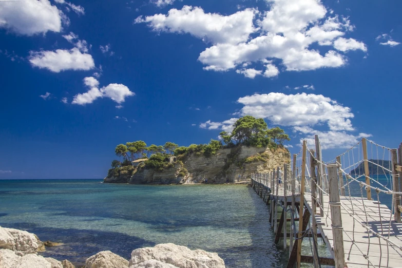 a wooden bridge over a body of water, a picture, shutterstock, romanticism, mediterranean island scenery, detailed trees and cliffs, stock photo, summer 2016