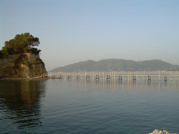 a body of water with a bridge in the background, flickr, mingei, calm sea, petros, very very very beautiful scenery, tansparent water