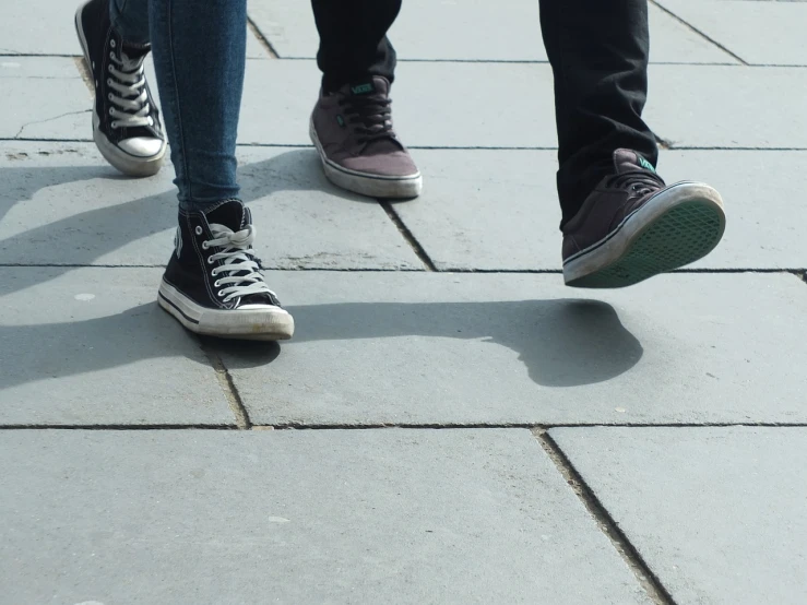 a couple of people standing next to each other on a sidewalk, pexels, realism, blue jeans and grey sneakers, floor tiles, teenagers, zoomed in shots