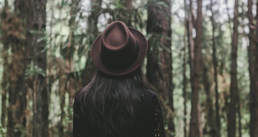 a woman wearing a hat standing in a forest, pexels, back of head, girl with dark brown hair, black stetson and coat, swirly dark hair