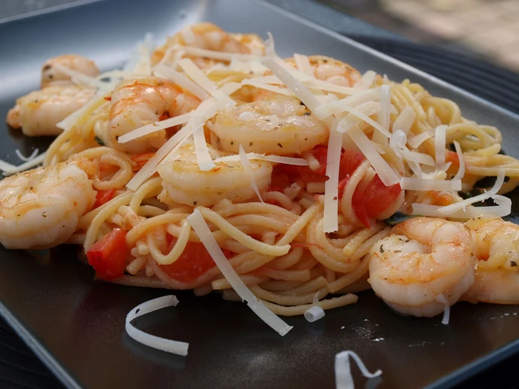 a black plate topped with pasta and shrimp, by Tom Carapic, closeup - view, beautiful sunny day, angled view, very romantic