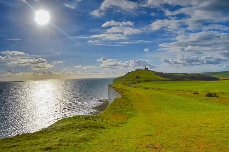 a grassy field next to a body of water, a stock photo, by Edward Corbett, shutterstock, cliffs of dover, bright sun, lighthouse, hdr photo