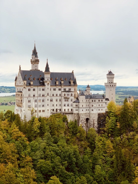 a castle sitting on top of a lush green hillside, by Emanuel Büchel, shutterstock, overlooking a vast serene forest, octoberfest, ivory towers, on a cloudy day