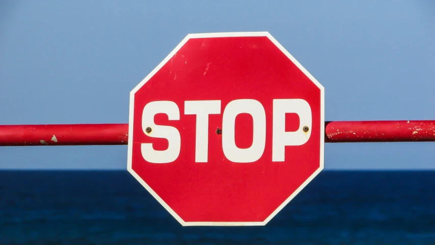 a red stop sign sitting on top of a metal pole, a picture, pixabay, sea, square, photograph credit: ap, looking threatening