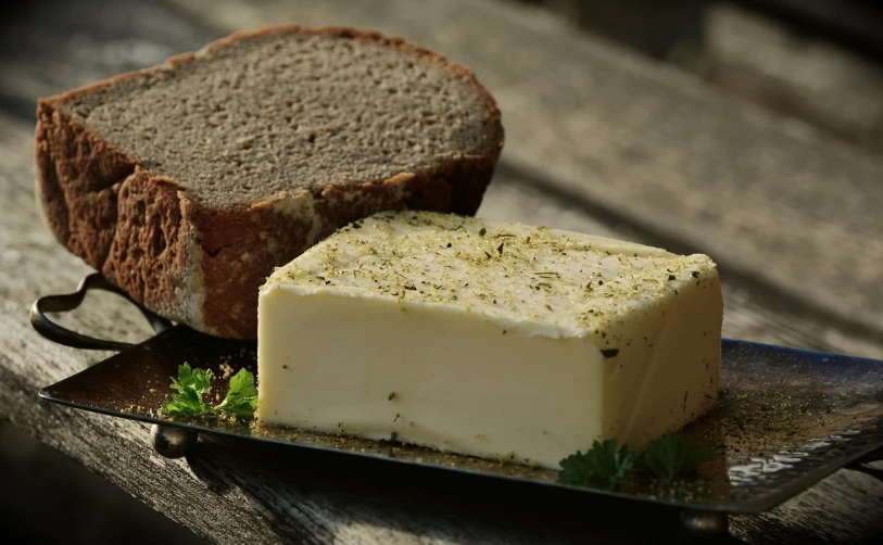a piece of bread sitting next to a piece of butter, a picture, by Dietmar Damerau, pixabay, herb, hillside, mozzarella, cubic