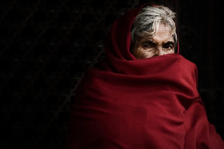 a woman wrapped up in a red blanket, inspired by Steve McCurry, pexels contest winner, old lady, intense dramatic hdr, mother of witchers, dressed in a sari