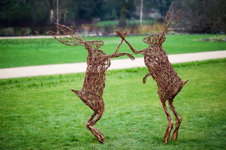 a couple of deer sculptures sitting on top of a lush green field, inspired by Patrick Dougherty, flickr, couple dancing, february), the wicker man, bird legs