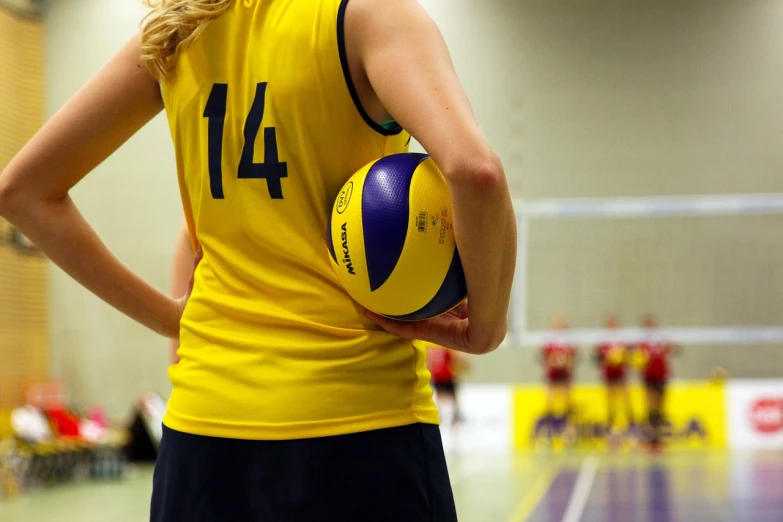 a woman in a yellow shirt holding a volleyball ball, a picture, by Christen Dalsgaard, shutterstock, back towards camera, afp, sleeveless, in blue and yellow clothes