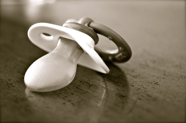 a baby pacifier sitting on top of a wooden table, by Etienne Delessert, flickr, sepia photography, soft white rubber, cone, patent