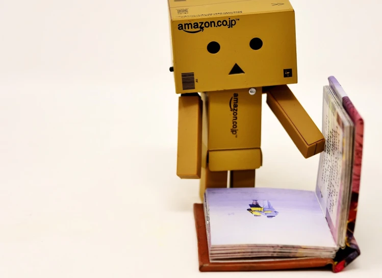 a cardboard robot standing next to an open book, a picture, by Randy Post, pixabay contest winner, dada, jeff bezos, cutie, [ everything is floating ]!!!, photo of a model