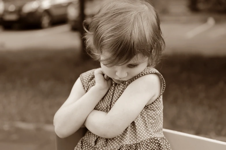 a little girl sitting on top of a wooden bench, by Lilia Alvarado, pexels, process art, facepalm, sepia toned, polka dot, arms crossed on chest