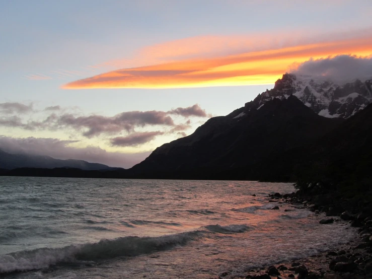 a body of water with a mountain in the background, a photo, by Charlotte Harding, flickr, burning clouds, patagonian, colorful swirly magical clouds, kanye