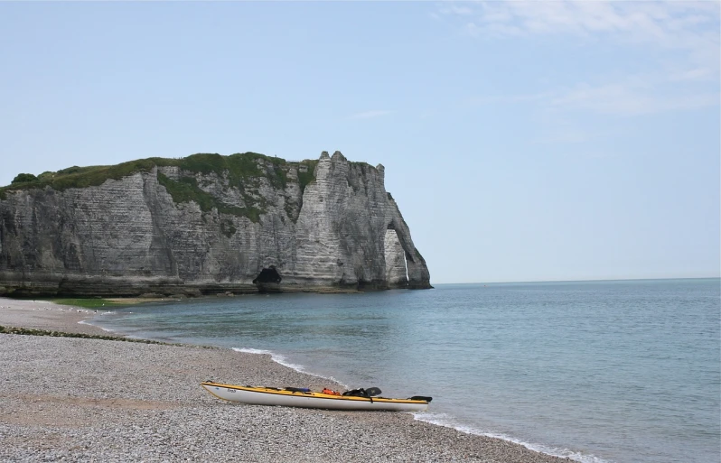 a yellow kayak sitting on top of a beach next to the ocean, a picture, by Edward Corbett, chalk cliffs above, traveling in france, benjamin vnuk, captain