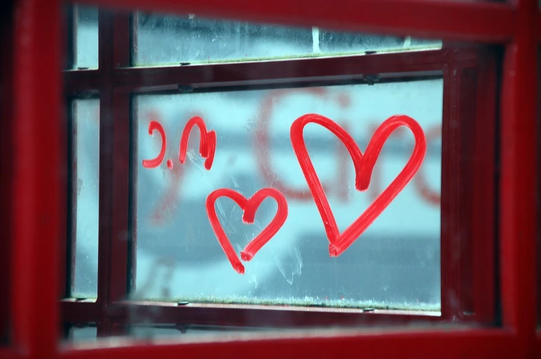 a red phone booth with two hearts drawn on it, a picture, viewed through the cars window, close up half body shot, header, bus