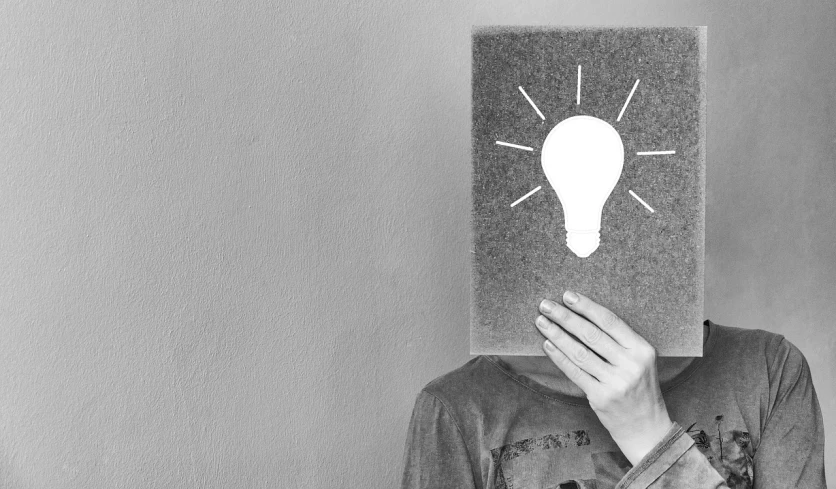 a person holding a piece of paper with a light bulb drawn on it, a black and white photo, pixabay, with a covered face, épaule devant pose, instagram picture, holding a giant book