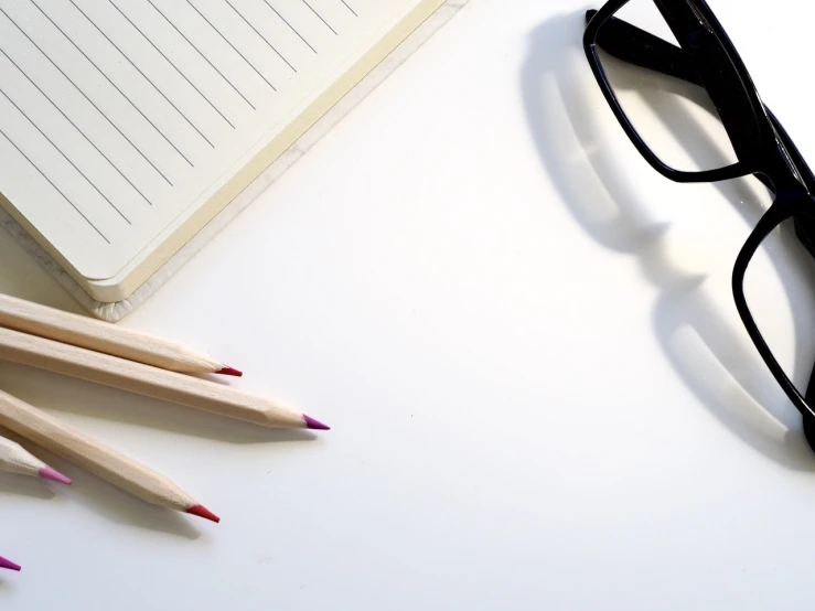 a pair of glasses next to a notebook and pencils, plain white background, sharpen lines, writing a letter, bold black lines