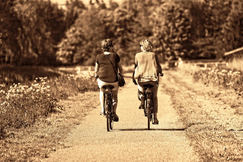 a couple of people riding bikes down a dirt road, by Caro Niederer, trending on pixabay, sepia sunshine, two women, back, relaxing