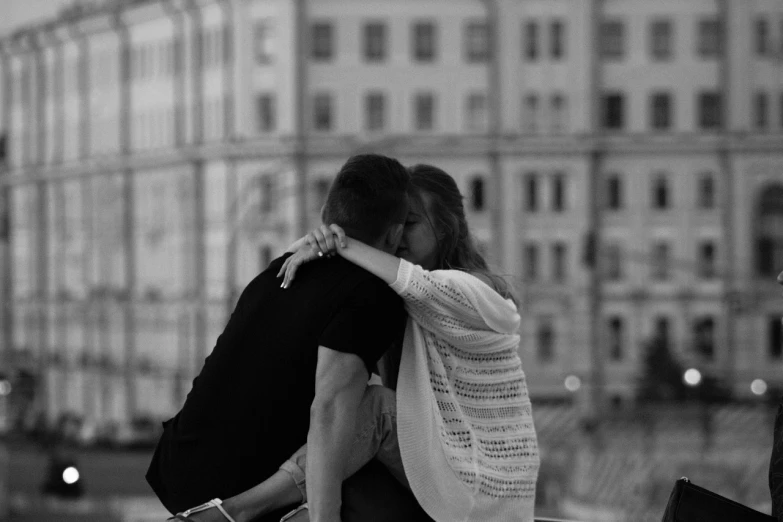 a black and white photo of two people sitting on a ledge, a black and white photo, unsplash contest winner, romanticism, peasant boy and girl first kiss, in moscow centre, summer evening, jesus hugging a woman