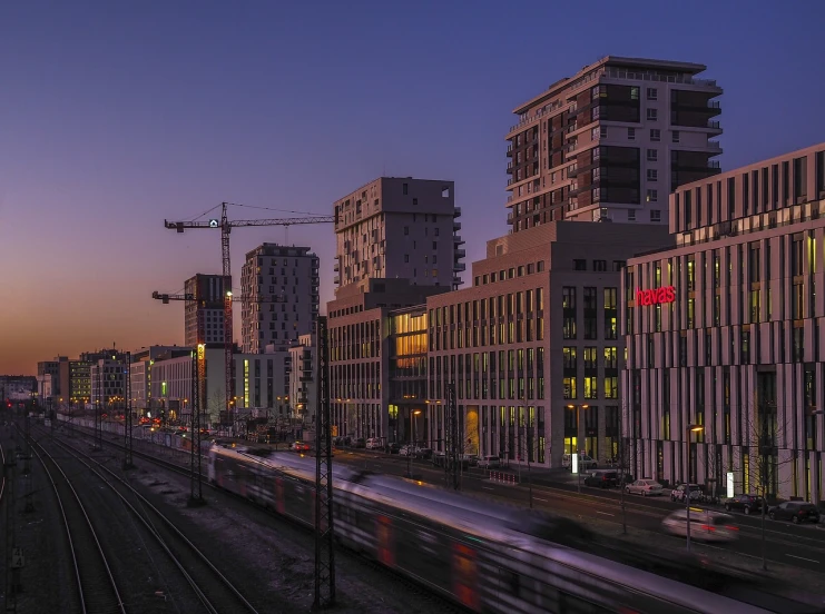 a train traveling through a city next to tall buildings, by Mathias Kollros, flickr, at dawn, espoo, real estate photography, construction