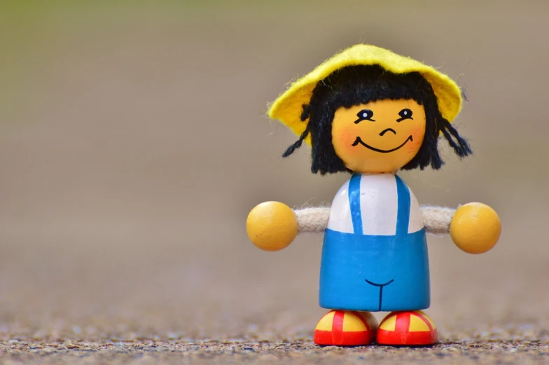 a close up of a toy with a hat on, a picture, pixabay contest winner, figuration libre, she is smiling and happy, half wooden pinocchio, standing in road, yellow and blue