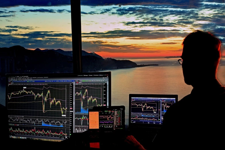 a man sitting in front of two computer monitors, romanticism, trading stocks, sunset view, monaco, high quality photo