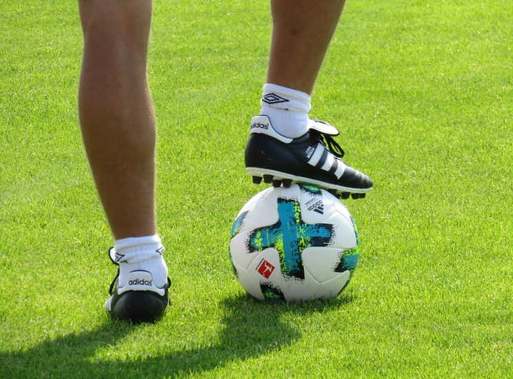 a person standing on top of a soccer ball, a picture, by Christen Dalsgaard, pixabay, gray shorts and black socks, green and white, elaborate detail, file photo