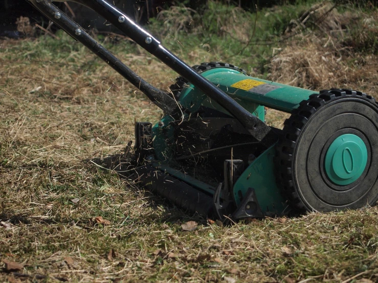 a green lawn mower sitting on top of a grass covered field, pixabay, realism, raking light, dry grass, panning shot, brutal violence