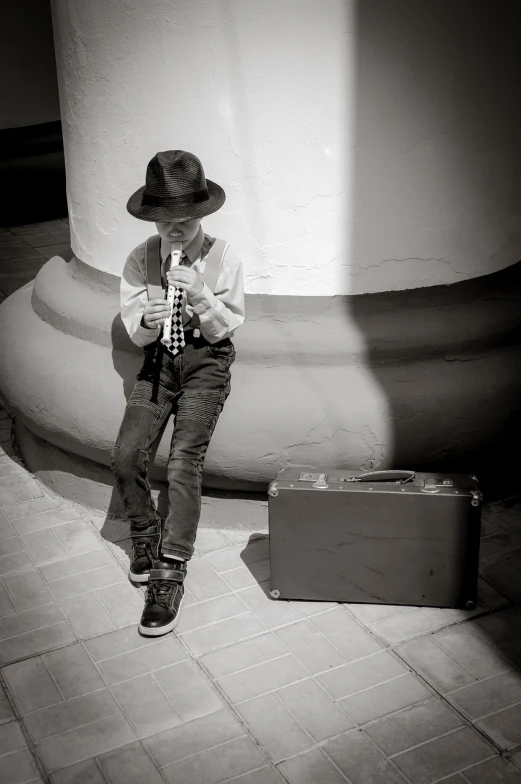 a young boy sitting on the ground next to a suitcase, a black and white photo, inspired by Henri Cartier-Bresson, pixabay contest winner, jamming to music, wearing a fedora, in style of mike savad”, rapping into microphone