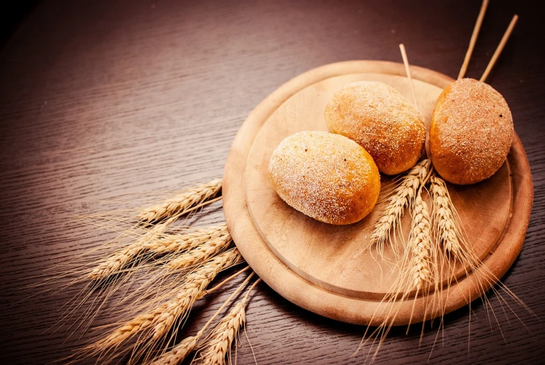 a wooden plate topped with three doughnuts on top of a wooden table, a stock photo, by Kazimierz Wojniakowski, shutterstock, folk art, wheat field, close macro photo. studio photo, with bread in the slots, 1970s photo