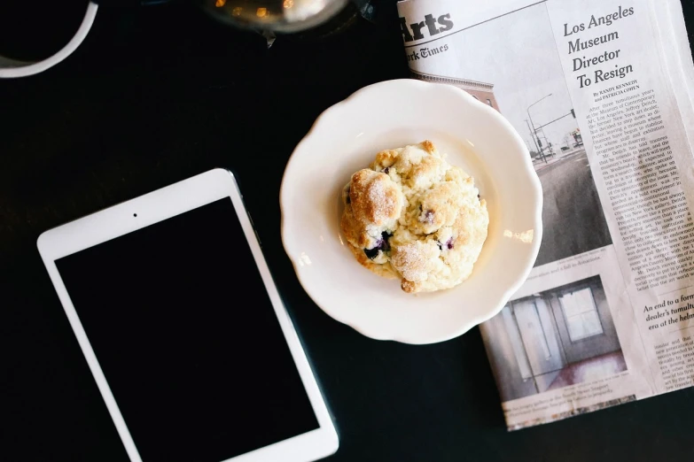 a white plate topped with a muffin next to a tablet, unsplash, technologies, blueberry, cafe in the clouds, journalistic photo