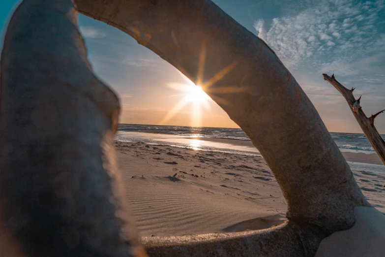 a piece of wood sitting on top of a sandy beach, a picture, by Sebastian Spreng, looking through a portal, sun rising, ultrawide lens, photo taken in 2 0 2 0