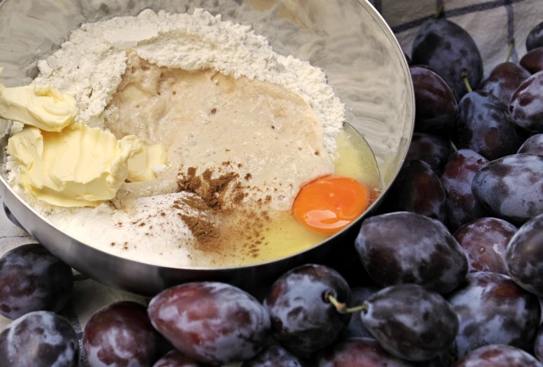 a bowl filled with batter next to a pile of plums, by Sylvia Wishart, pixabay, covered in white flour, work in progress, grape, butter