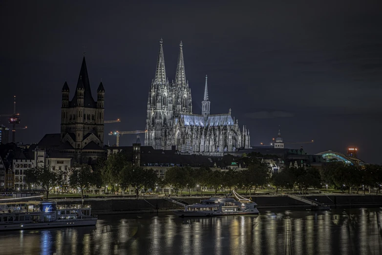 a large cathedral towering over a city next to a river, by Sebastian Spreng, photography at night, majestic spires, very very well detailed image, soft filmic tonemapping