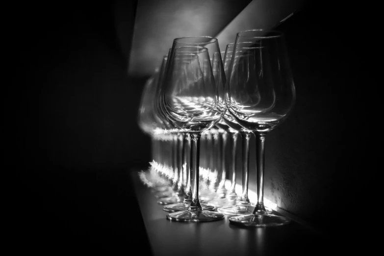 a row of wine glasses sitting on top of a table, a black and white photo, minimalism, dramatic backlit lighting, dark kitchen of an art student, high details photo