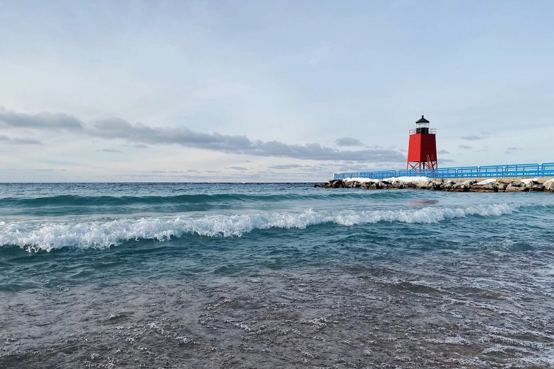 a lighthouse in the middle of a body of water, a picture, by Jacob Burck, beach pic, michigan, red peaks in the background, perfect spring day with