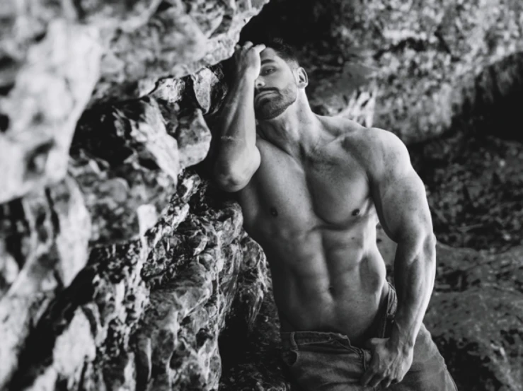 a shirtless man leaning against a rock, a black and white photo, by Adam Dario Keel, his palms are sweaty, muscled, editorial photo from magazine, instagram photo