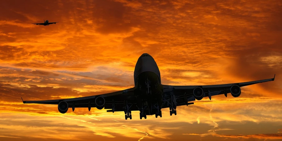 a large jetliner flying through a cloudy sky, pixabay contest winner, the glimmering orange dawn, silhouette!!!, in front of an orange background, full body close-up shot